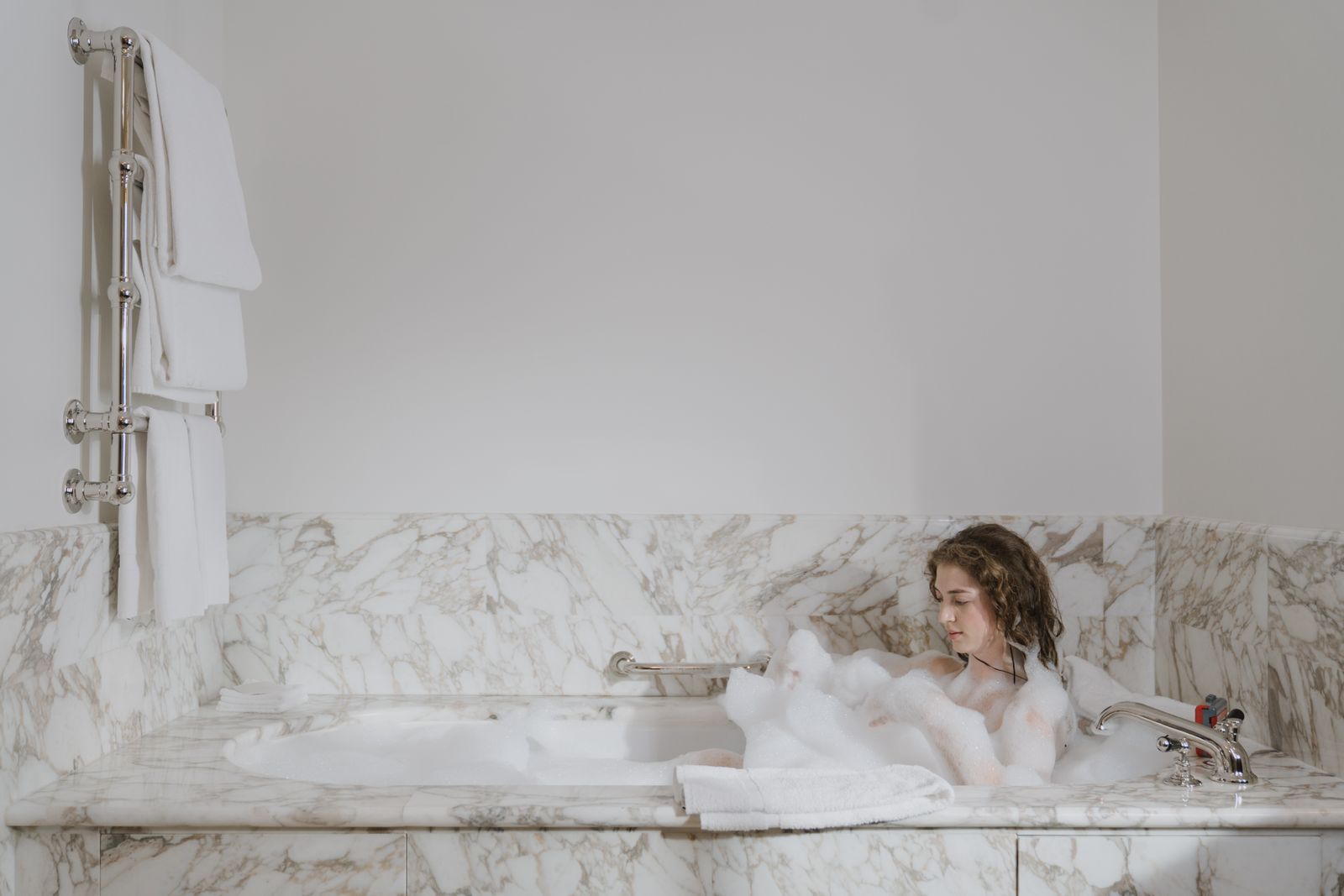Woman relaxing in a bubble bath in a marble bathroom